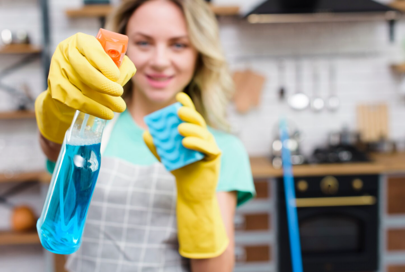 Young female cleaner showing detergent spray bottle
